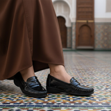 Mocassin noir verni avec jellaba marron dans intérieur marocain