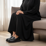 Woman in black matte djellaba sitting gracefully with soft daylight wearing 306F Nexa Noir loafers