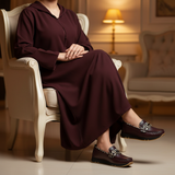 Woman in burgundy matte djellaba seated elegantly with warm night lighting wearing 490F Zahir Bordeaux loafers