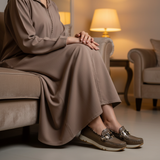 Woman in taupe matte djellaba sitting gracefully with warm night lighting wearing 490F Zahir Sépia loafers